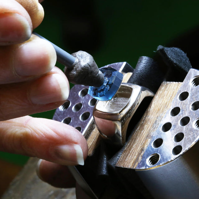 An intaglio stone with a mermaid design carved on it is being set on a white gold ring.